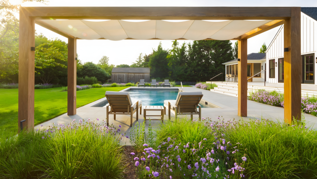Retractable fabric pergola providing shade over poolside seating area at a modern backyard patio with landscaped garden and outdoor living space