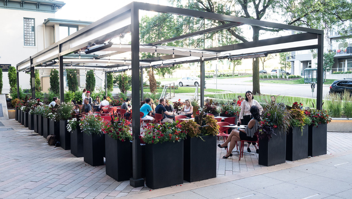Modern Commercial Outdoor Dining Pergola with Retractable Shade Canopy Modern outdoor restaurant patio featuring a commercial pergola structure with retractable shade canopies, string lighting, landscaped planters, and guests dining outdoors.