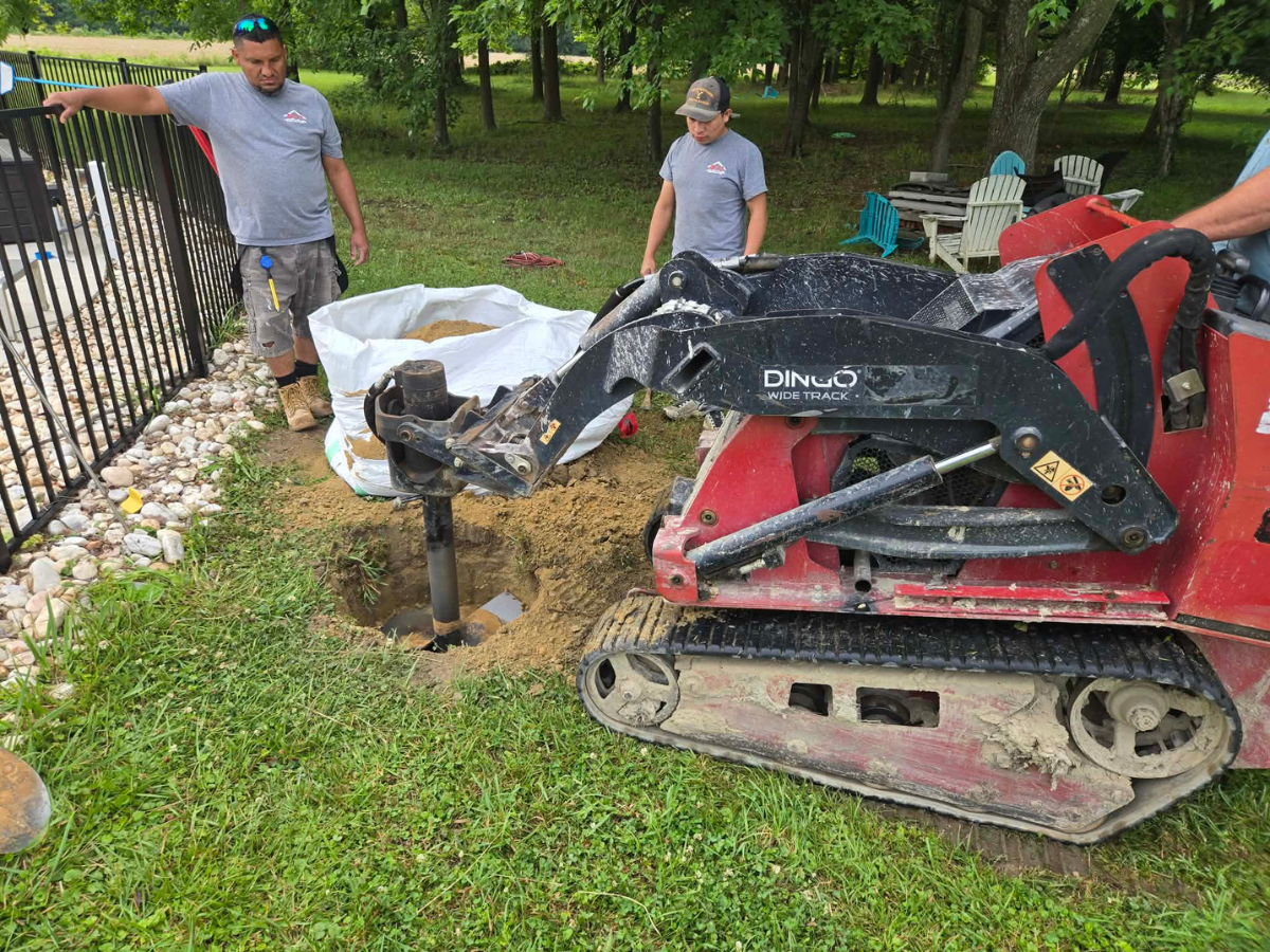Excavating foundations for heavy-duty steel support posts beside a residential swimming pool.