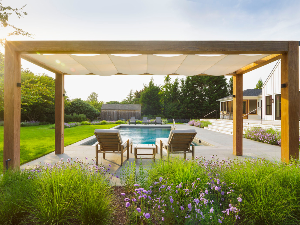 Modern pergola creating shade beside a residential swimming pool and outdoor seating area.