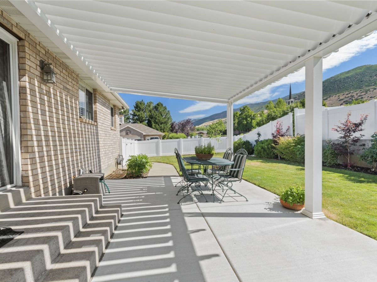 Modern white louvered pergola creating adjustable shade over a backyard patio.