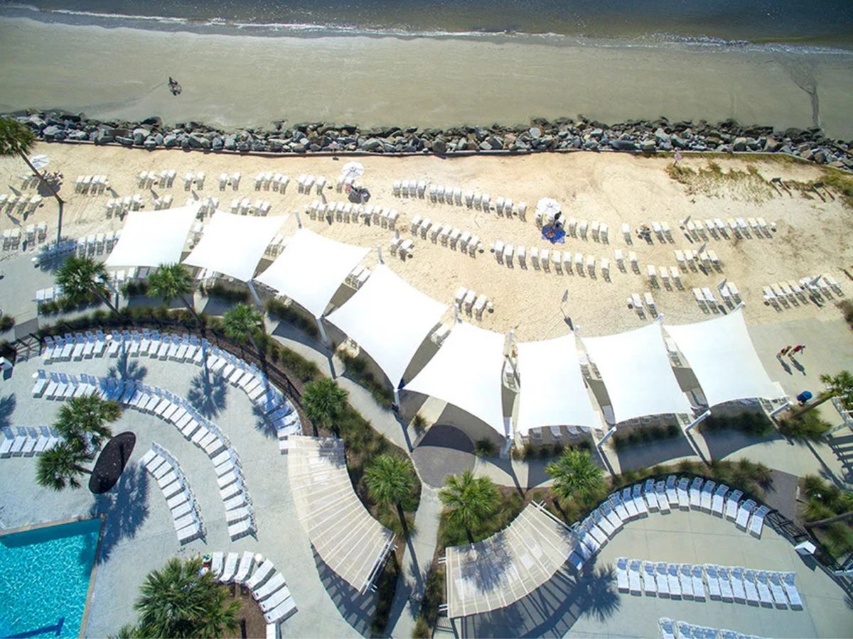 Custom commercial shade sails providing shade over a beachfront resort seating area.