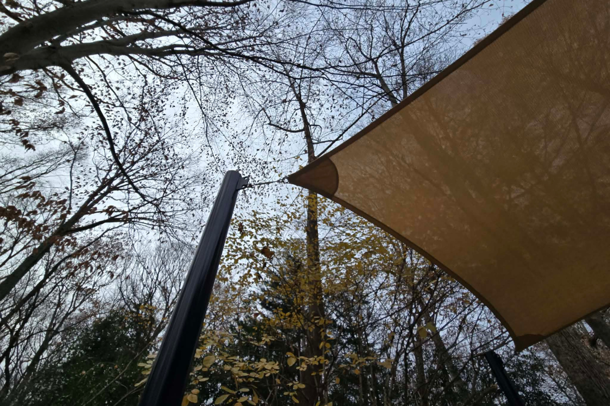 Cable and attachment hardware being inspected for seasonal wear. Shade sail corner, cable, and attachment hardware being inspected for seasonal wear.