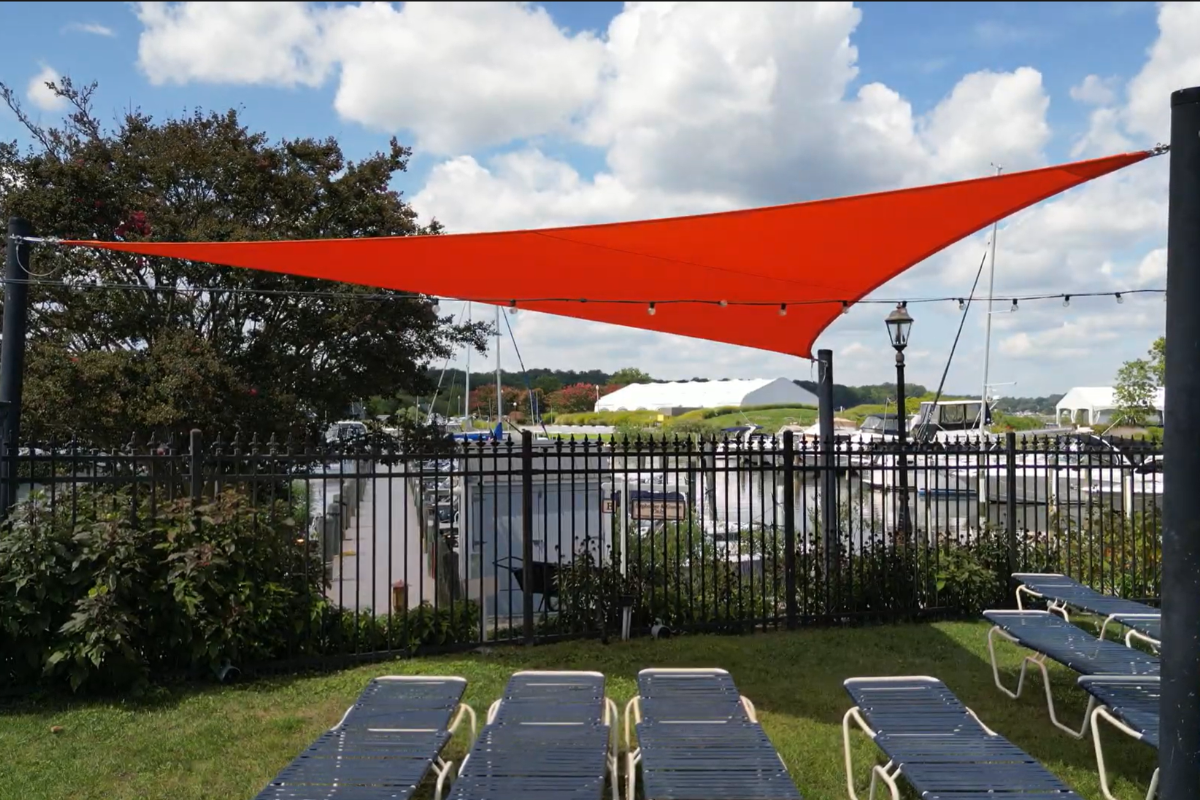 View beneath orange shade sail providing shade over lounge chairs at a Maryland marina